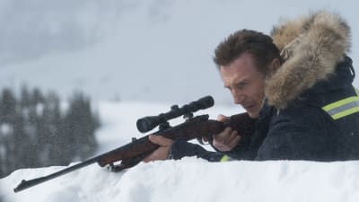LIam Neeson ligger i snön och siktar med ett gevär.