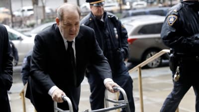 Harvey Weinstein går framåt med rullator. I bakgrunden syns polis.