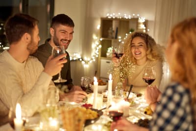 Fyra leende personer vid ett matbord. De har vinglas i händerna och på bordet finns många stearinljus. I bakgrunden en hylla och ljusslingor.