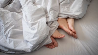 Närbild på två par fötter som sticker ut under ett täcke. 