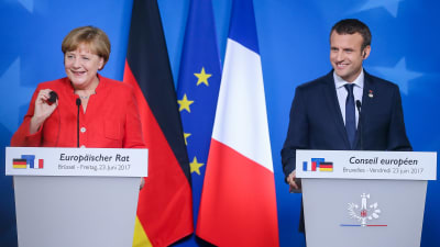 Tysklands förbundskansler Angela Merkel och Frankrikes president Emmanuel Macron ler bakom sina podium med Tysklands, EU:s och Frankrikes flagga i bakrgunden på EU-toppmötet.