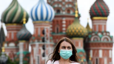 Långhårig kvinna bär ansiktsskydd framför ortodoxa kyrkkupoler.
