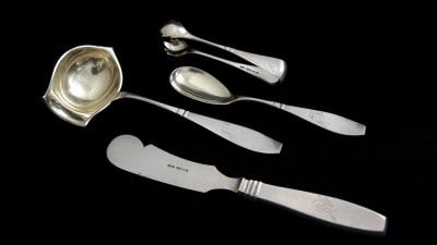 En sockertång, en såsslev, en smörkniv och en sked i silver.