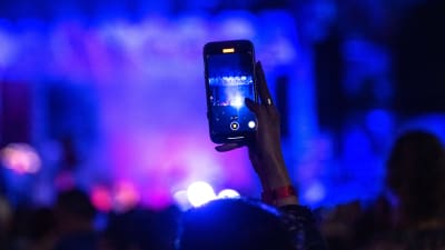 Närbild av en persons hand som filmar med en Iphone på en konsert.