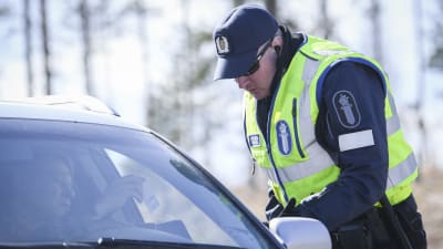 En polis kontrollerar körkortsuppgifter hos en person i en personbil.