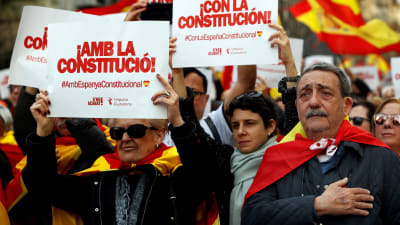 Demonstranter iklädda Spaniens flagga håller upp skyltar med texten "med konstitutionen" .