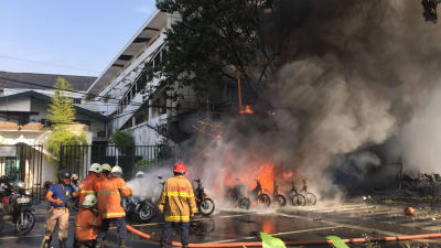 Brandmän släcker branden utanför polishögkvarteret i Surabaya efter självmordsattacken där. 