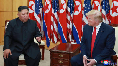 Pohjois-Korean johtaja Kim Jong-un ja Yhdysvaltain presidentti Donald Trump istuvat maiden lippujen edessä ja keskustelevat