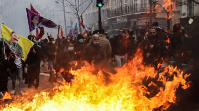 Domstranter på gatan i Paris, framför dem stora eldlågor.
