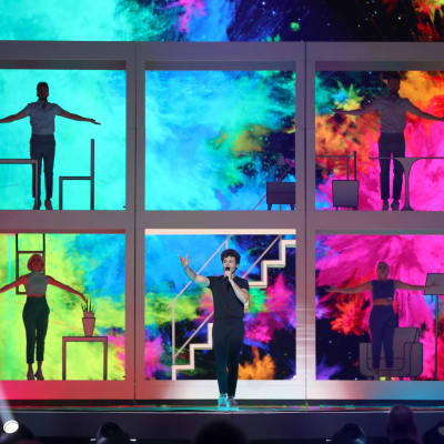 miki uppträder för spanien med färgglad bakgrund och ett stort fönster med sångare i i bakgrunden