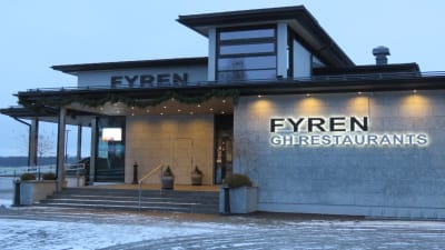 En restaurang, fasaden fotad en grå eftermiddag i januari. Finns i Norra hamnen i Ekenäs. Byggnaden går i grått och svart. Står Fyren GH restaurants på fasaden.