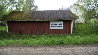 Skylt på rött uthus i Hanhikivi by, tassarna bort från Hanhikivi
