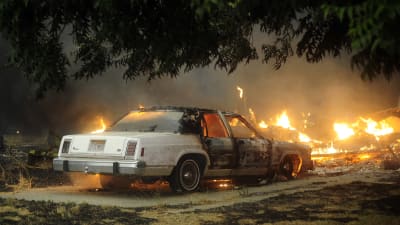 En nedbränd bil omgiven av lågor