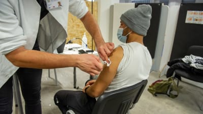 Sjukskötare vaccinerar en ung man iklädd munskydd. 