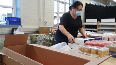 Porträtt av en kvinna som organiserar lådor med matprodukter i ett förråd. 
