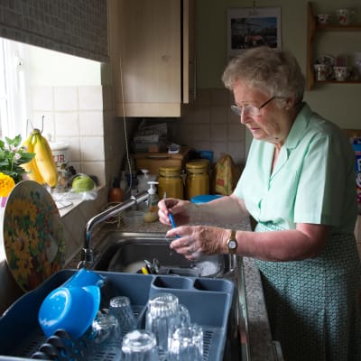 En pensionär som bor ensam står vid dsikhon i sitt kök.