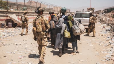 Soldater går bredvid en grupp som ska evakueras från Kabuls flygplats och styr dem dit de ska.