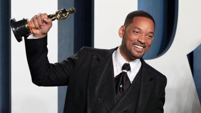 Will Smith klädd i kostym ler medan han poserar med sin Oscarsstatyett på röda mattan.