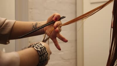 Handen av en frissa som håller i en sax och klipper hår. 