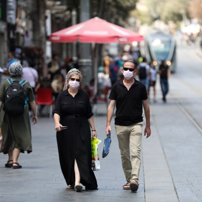 Människor med ansiktsskydd som promenerar på en gata i Jerusalem.