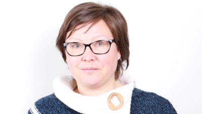 En kvinna i kort mörkt hår och glasögon tittar in i kameran.