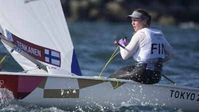 Tuula Tenkanen seglar i sin båt med Finlands flagga och namnet på seglet.