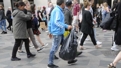 Flasksamlare med en stor svart plastsäck i folkvimlet på en gata.