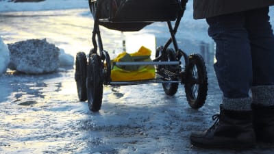 En person skuffar fram en barnvagn på en isig väg.