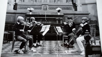 Ett svartvitt foto på en kvartett med fyra pojkar sitter på varsin stol och spelar violin.