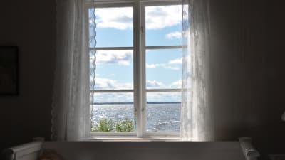Havsutsikt från ett fönster. Vita tyllgardiner, sommar, glittrande hav.