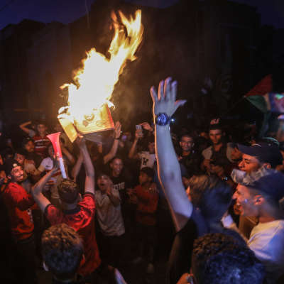 Ett stort antal män har samlats för att fira. En del håller i palestinska flaggor. Någon håller i något som brinner och en tuta.