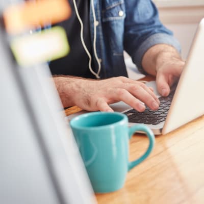 En man som skriver på en laptop. Bredvid honom står en kaffekopp. 