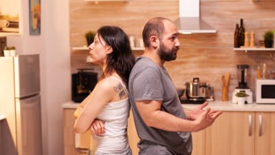 En kvinna och en man står rygg mot rygg i ett kök. 