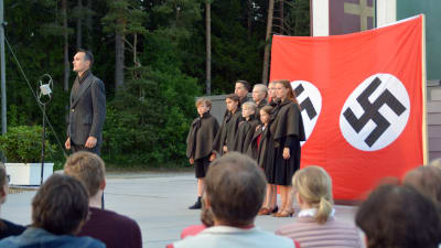 Familjen von Trapp sjunger på scenen. I bakgrunden syns en nazistflagga. Från vänster: Leif Wadenström, Simon Wadenström, Birk Lerviks, Inka Lounela, Felicia Wadenström, Minea Korenius, Emilia Ekström, Ellen Haakana och Sarah Nedergård.