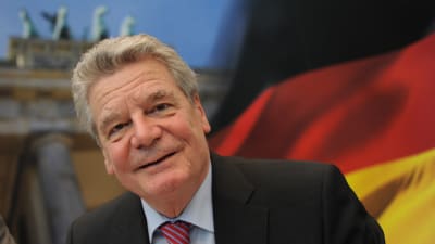 Joachim Gauck, en gråhårig leende man, framför en tysk flagga.
