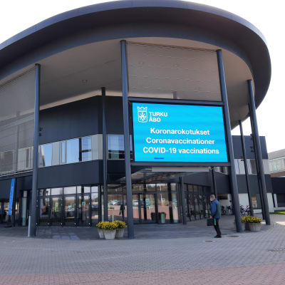 En blå lysande skylt berättar att du ska gå in här för coronavaccinering i Åbo mässcentrum.
