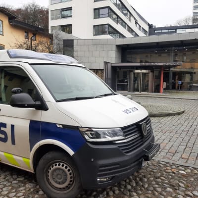 En polisbil står parkerad på en stenlagd innergård vid ett hus med glasväggar. Ovanför ingången står Turun oikeustalo Åbo rättscenter.