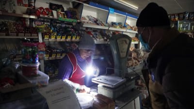 En kund och en försäljare i en mörk kiosk håller upp en ficklampa vid kassan.