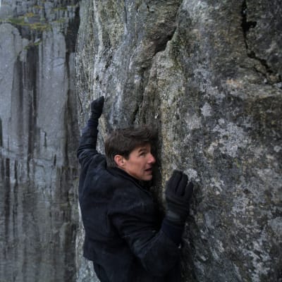 Ethan Hunt (Tom Cruise) klänger sig fast på en hög klippvägg.
