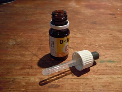 D-vitamindroppar i brun flaska på brunt bord.
