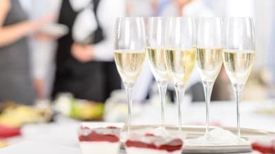 En bricka med champagne eller mousserande vin står på ett bord. I bakgrunden synd flera personer i festkläder.
