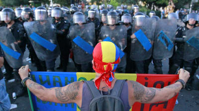 Demonstrant håller upp plakat framför en rad rumänska poliser i Bukarest.  