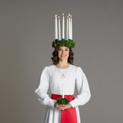 Finlands lucia 2019 Sara Ray iklädd luciakrona med tända ljus och vit särk med rött band.