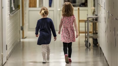 Två unga flickor går i en korridor.