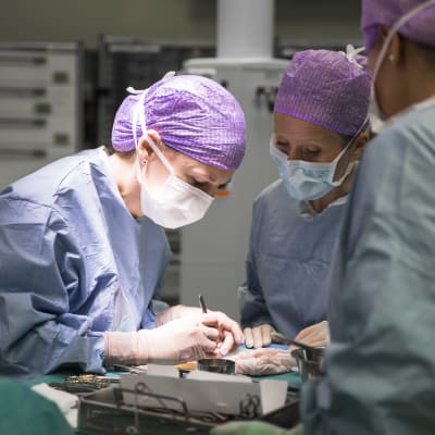 Kolme terveydenhuollon ammattilaista suorittaa leikkausta.