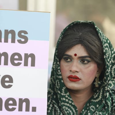 En sminkad demonstrant i huvudduk med med en skylt med texten "Trans women are women", alltså "Transkvinnor är kvinnor".