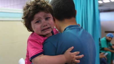 Ett gråtande barn i förs i famnen på en man i ett sjukhus.