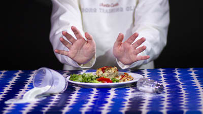 Symbolbild där två händer skuffar bort en tallrik med mat. Ett glas med mjölk välter ut över bordet. 
