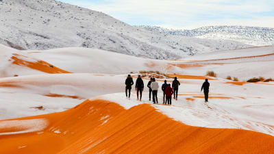 Människor vandrar på snötäckta sanddyner.