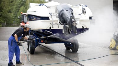 En man tvättar båtbotten med vatten.
